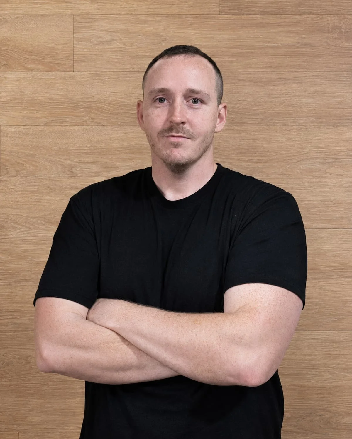 Dr Joshua Saxton, Adelaide osteopath and Accredited Exercise Physiologist, standing with his arms crossed in a gym.