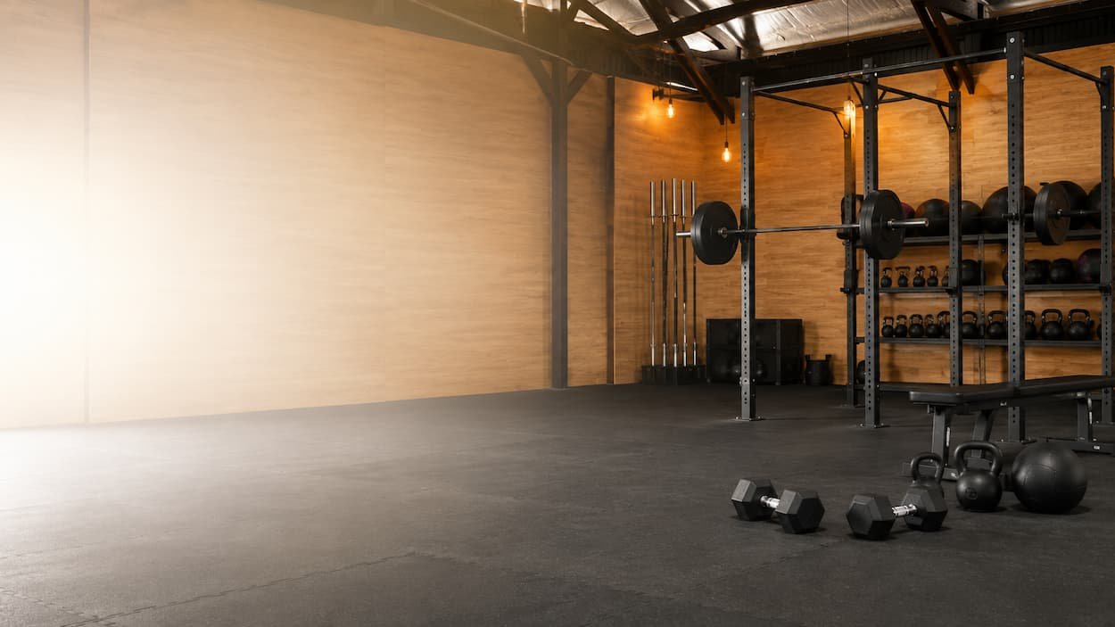 Empty gym with weightlifting equipment, including barbells, dumbbells, kettlebells, and resistance bands.