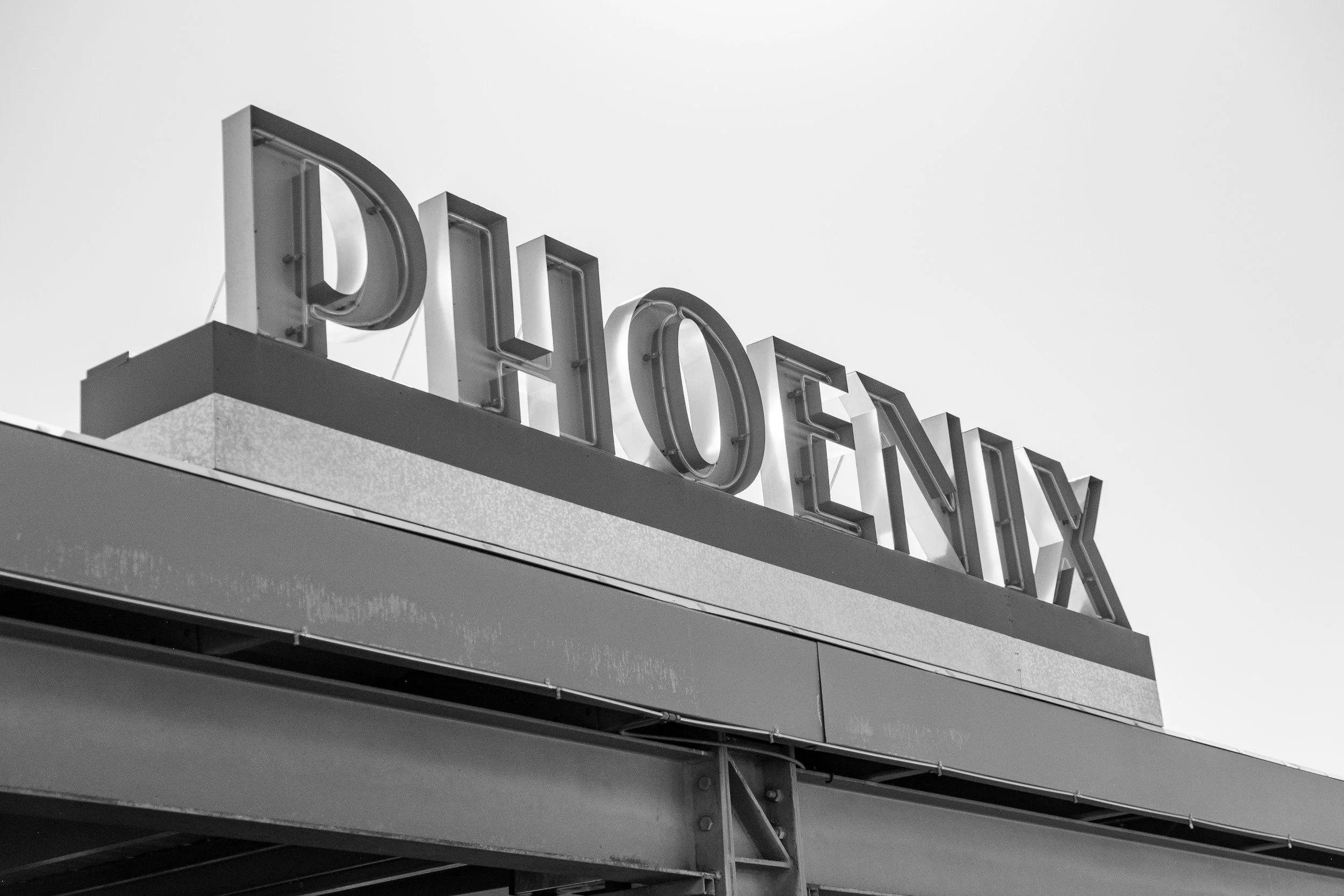 Black and white photo of a building corner with large illuminated letters spelling 'The'. the perspective is from below, looking up at the sign.