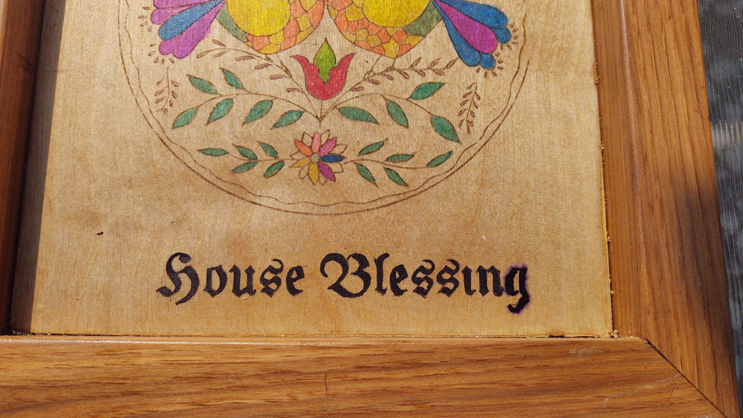 Close-up of a wooden puzzle box with the words "Source Blessing" and a colorful embroidered design of a bird and flowers on it, placed on a wooden surface.