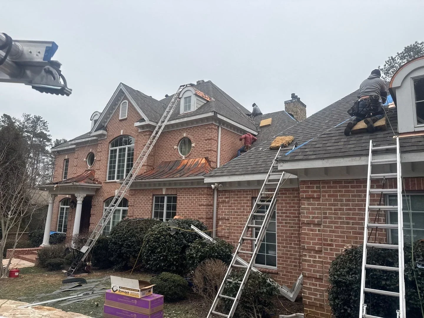 Brick two-story home with copper accents, receiving a new roof with asphalt shingles and custom hooded gutter guards