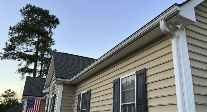 Gutters with custom aluminum gutter guards on house with siding and asphalt shingles and American Flag hanging from porch