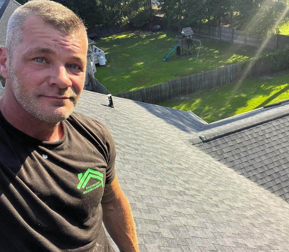 A man taking a selfie on a house roof with a backyard and a wooden playset visible in the background.