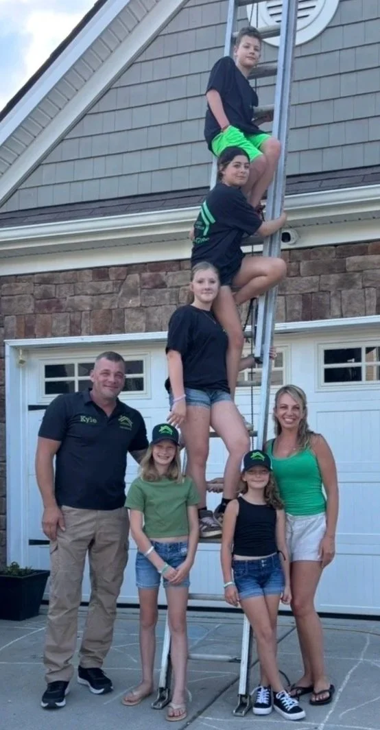 Kyle McLean Roofing and Repair Family posing by ladder next to house