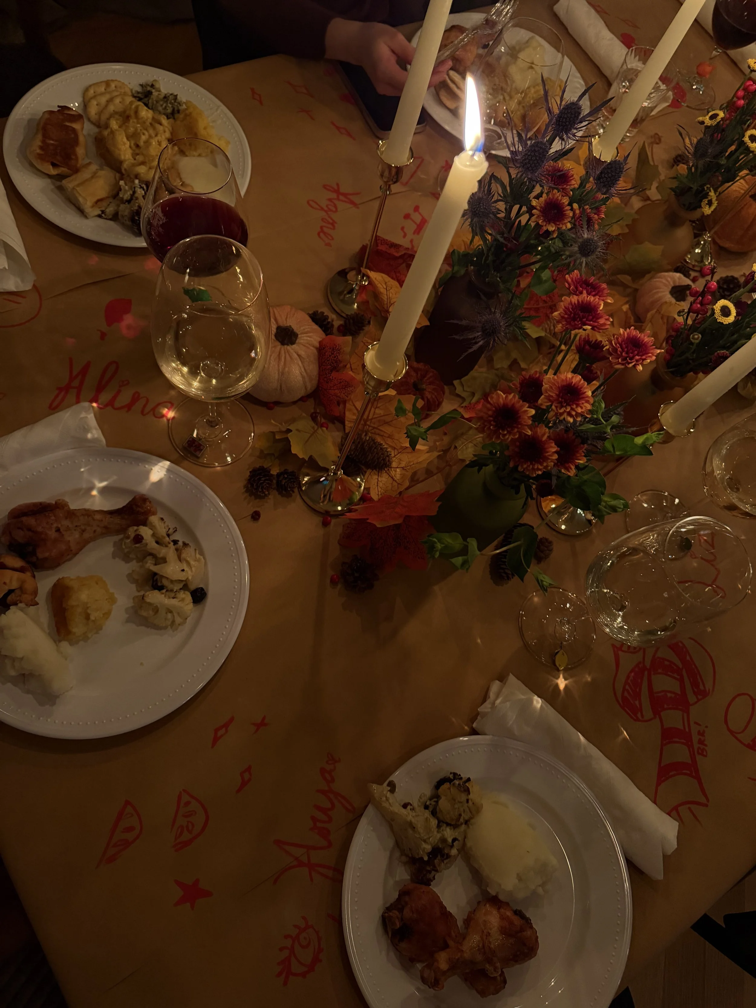 A dinner table with plates of food, wine glasses, candles, and fall-themed decorations including pumpkins and flowers.
