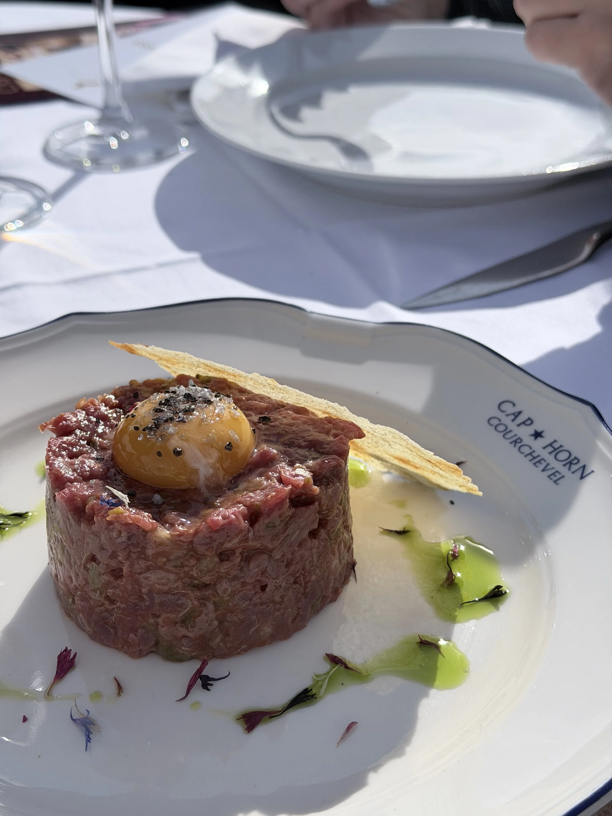 A plate with steak tartare topped with a raw egg yolk, served with edible flowers and drizzled with green oil or sauce.