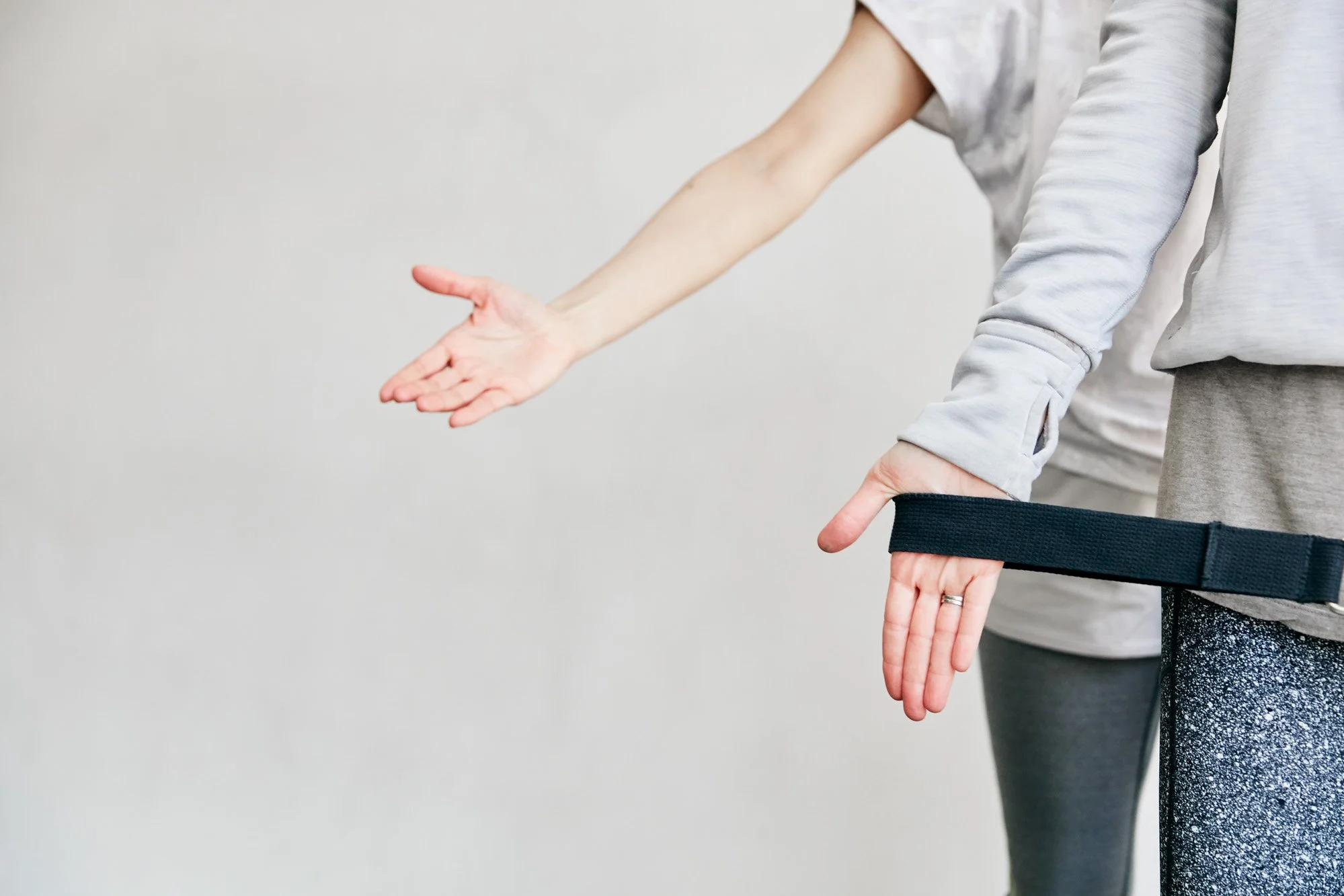 Person demonstrating a physical stretch or exercise with arms extended and fingers pointing downward, wearing a gray long-sleeve shirt and gray sweatpants.