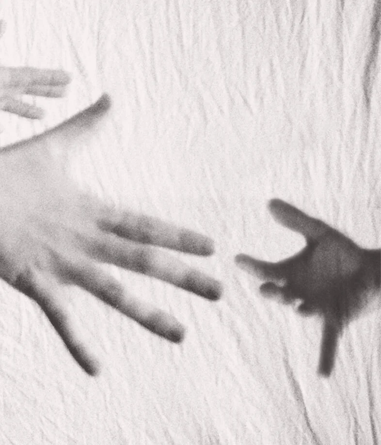 Black and white photo of two hands reaching towards each other near a textured wall.