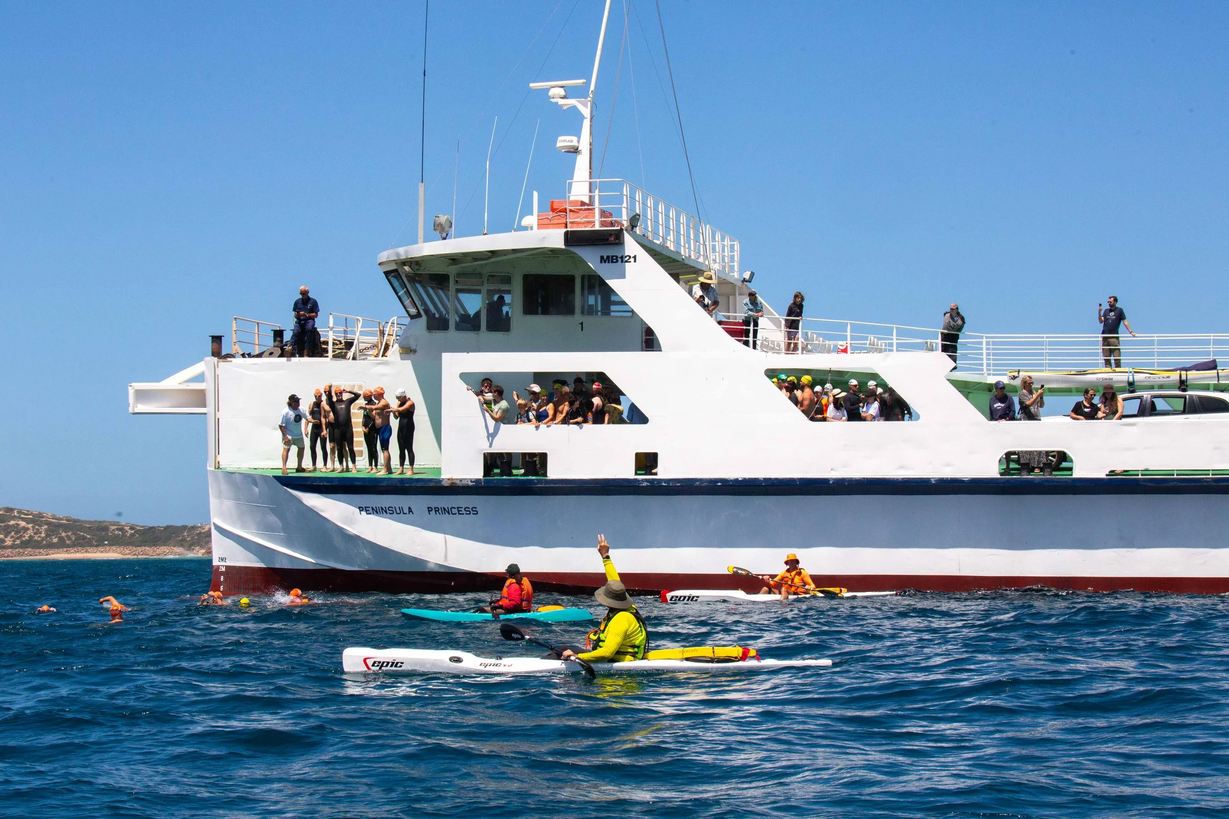 People swimming and kayaking in the water near a large white boat named 'Peninsula Princess' with a clear blue sky in the background.