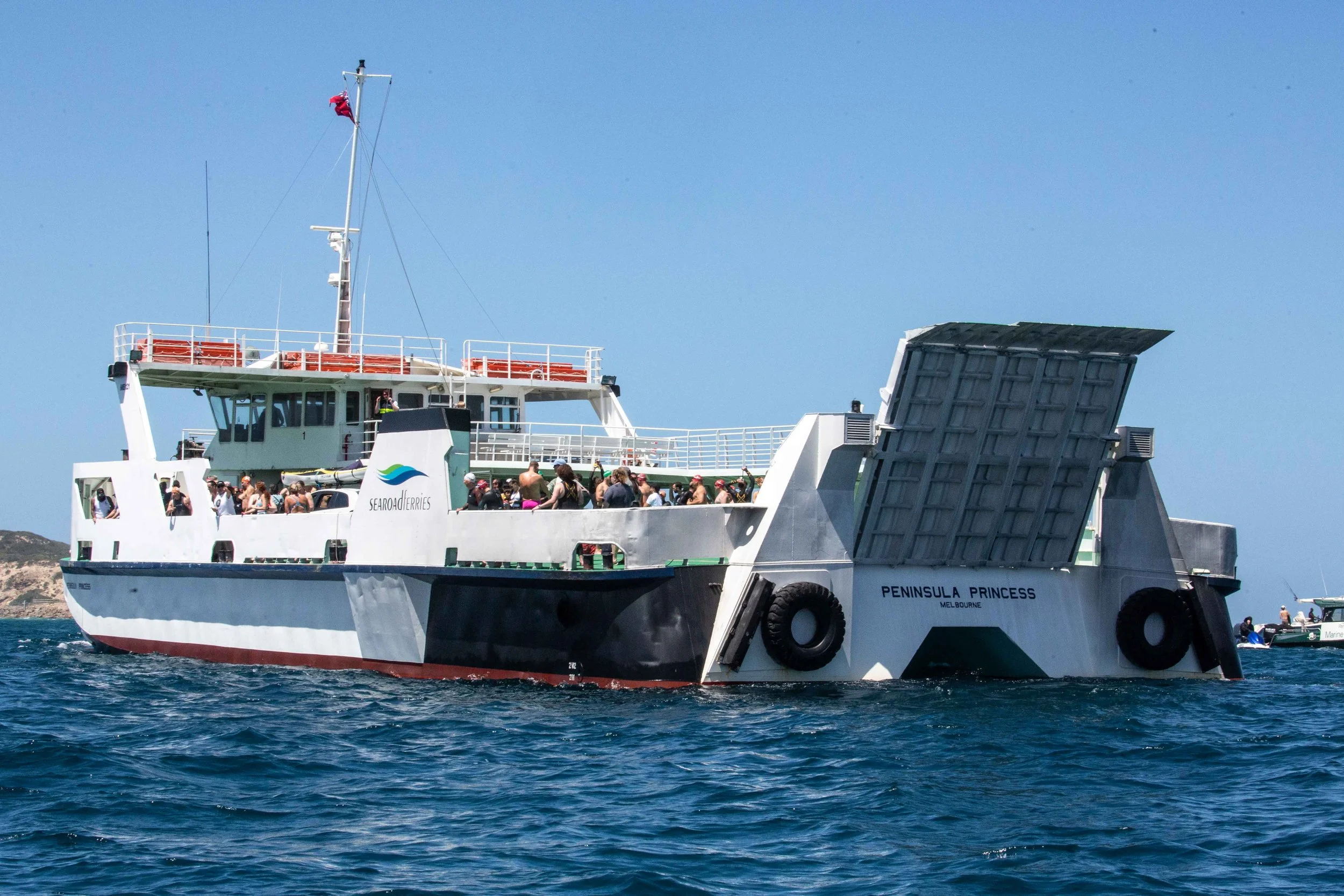 A large ferry boat named Peninsula Princess with passengers on board, docked at a port with a vehicle loading ramp open, under a clear blue sky.