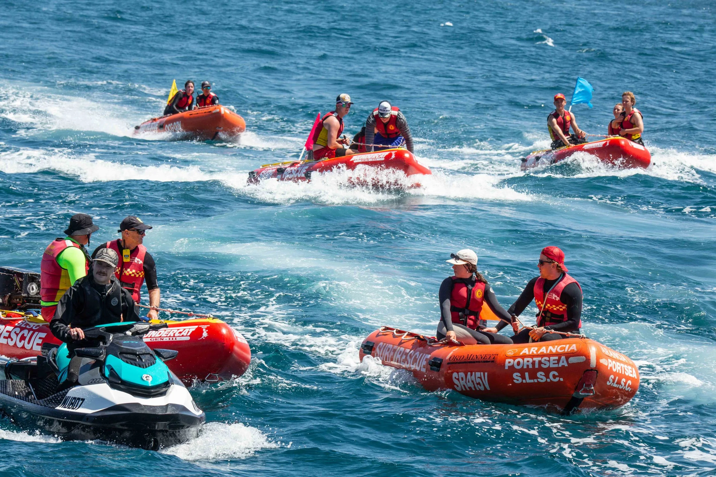 A group of emergency rescue personnel on inflatable rescue boats and jet skis in the ocean, engaging in a rescue operation or training exercise.
