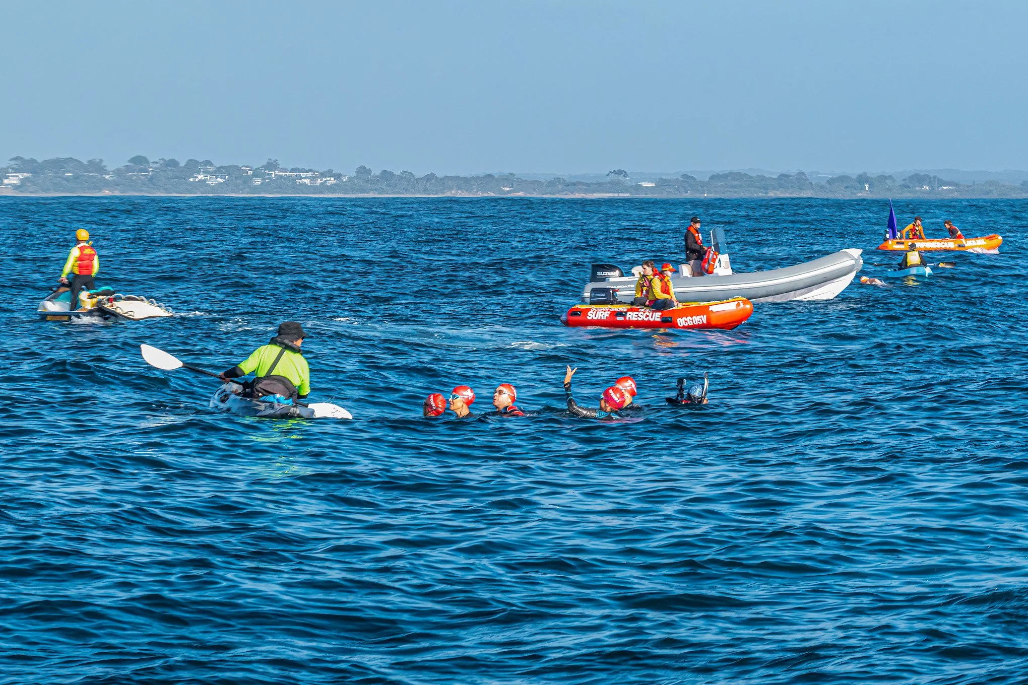 Group of people in life jackets participating in water rescue training exercises with boats and rescue equipment on a large body of water.
