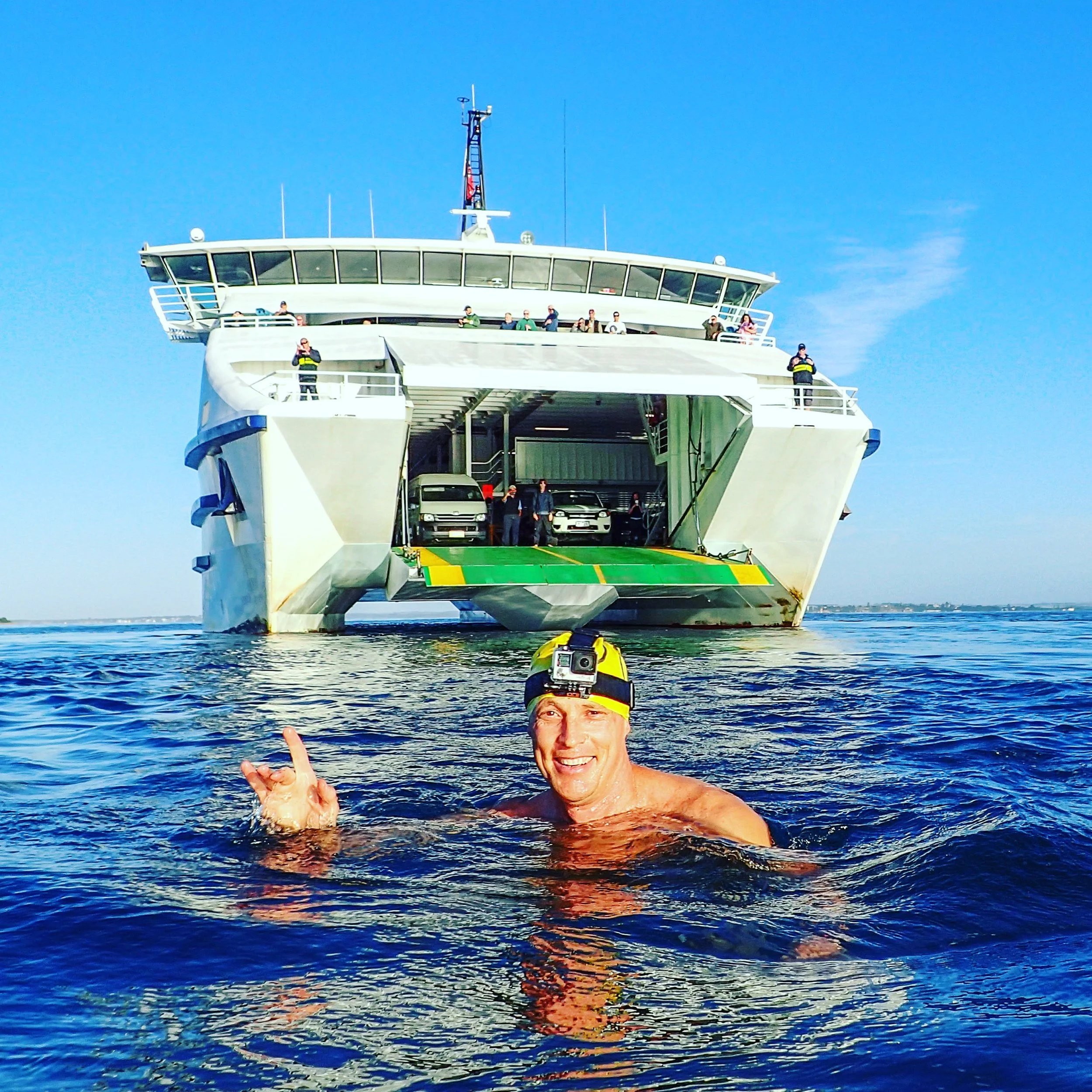Grant Siedle in the water smiling. Behind him is the Searoad passenger ferry that he has just jumped off to begin a swim!