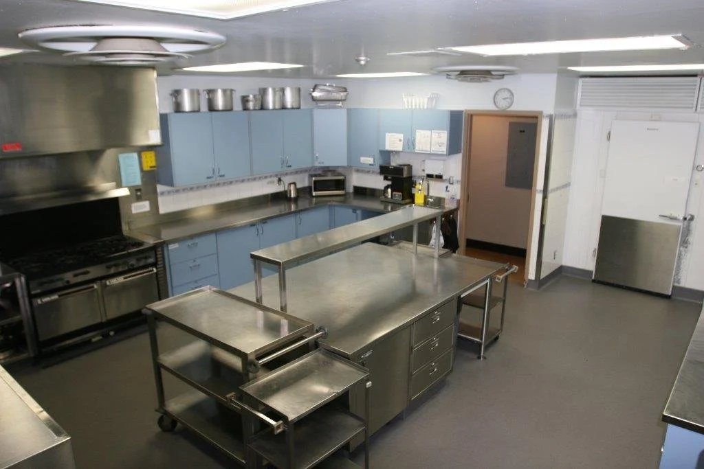 Empty industrial kitchen with blue cabinets, stainless steel countertops, and cooking appliances.