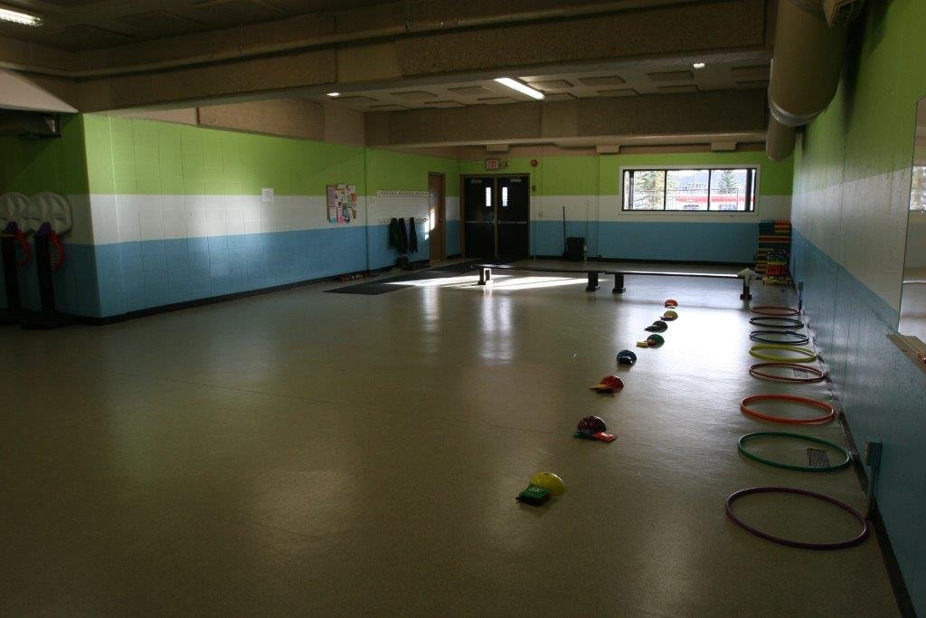 Empty indoor room with colorful walls, therapy balls, and hoops along the right side, likely a physical therapy or activity room for children.