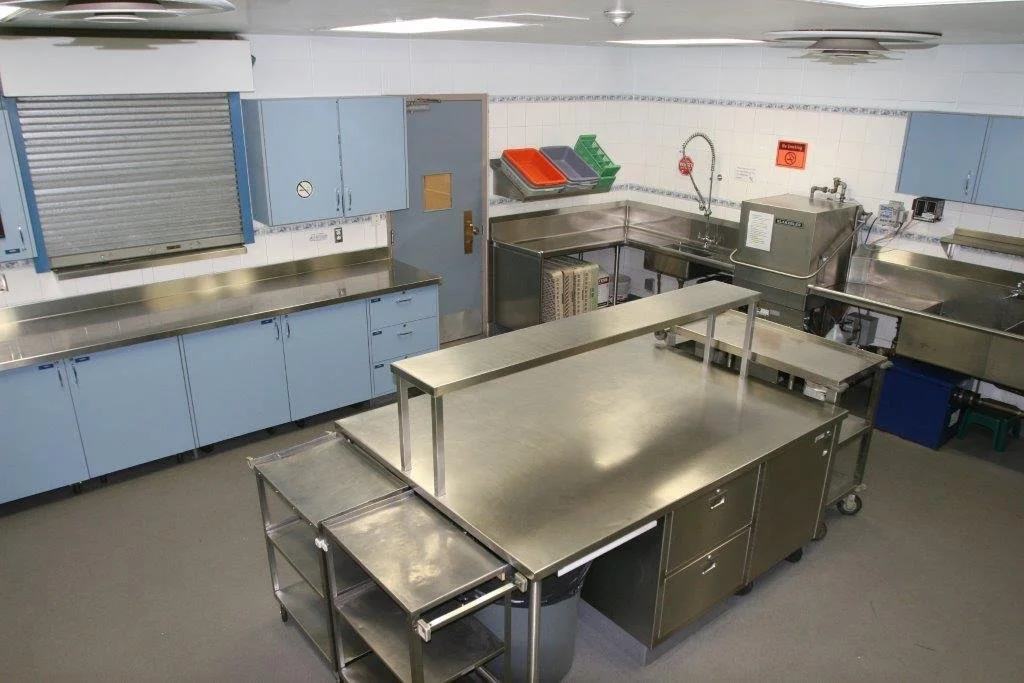 Commercial kitchen with stainless steel counters, sink, and equipment, blue cabinets, and a closed rolling door.