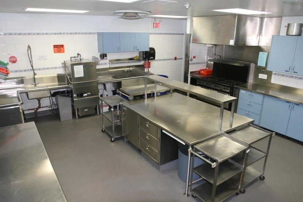 Empty commercial kitchen with stainless steel counters, blue cabinets, and kitchen appliances.