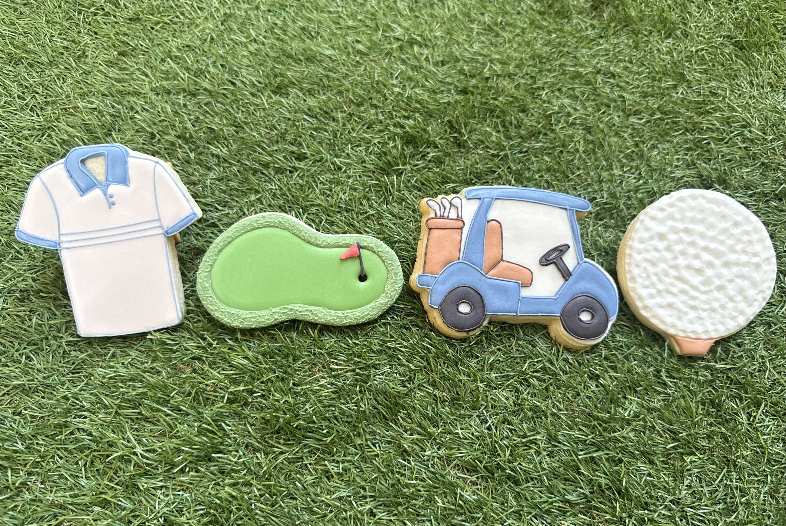 Cookies decorated with golfing theme designs including a golf shirt, a golf hole with a flag, a golf cart, and a golf ball on green grass.