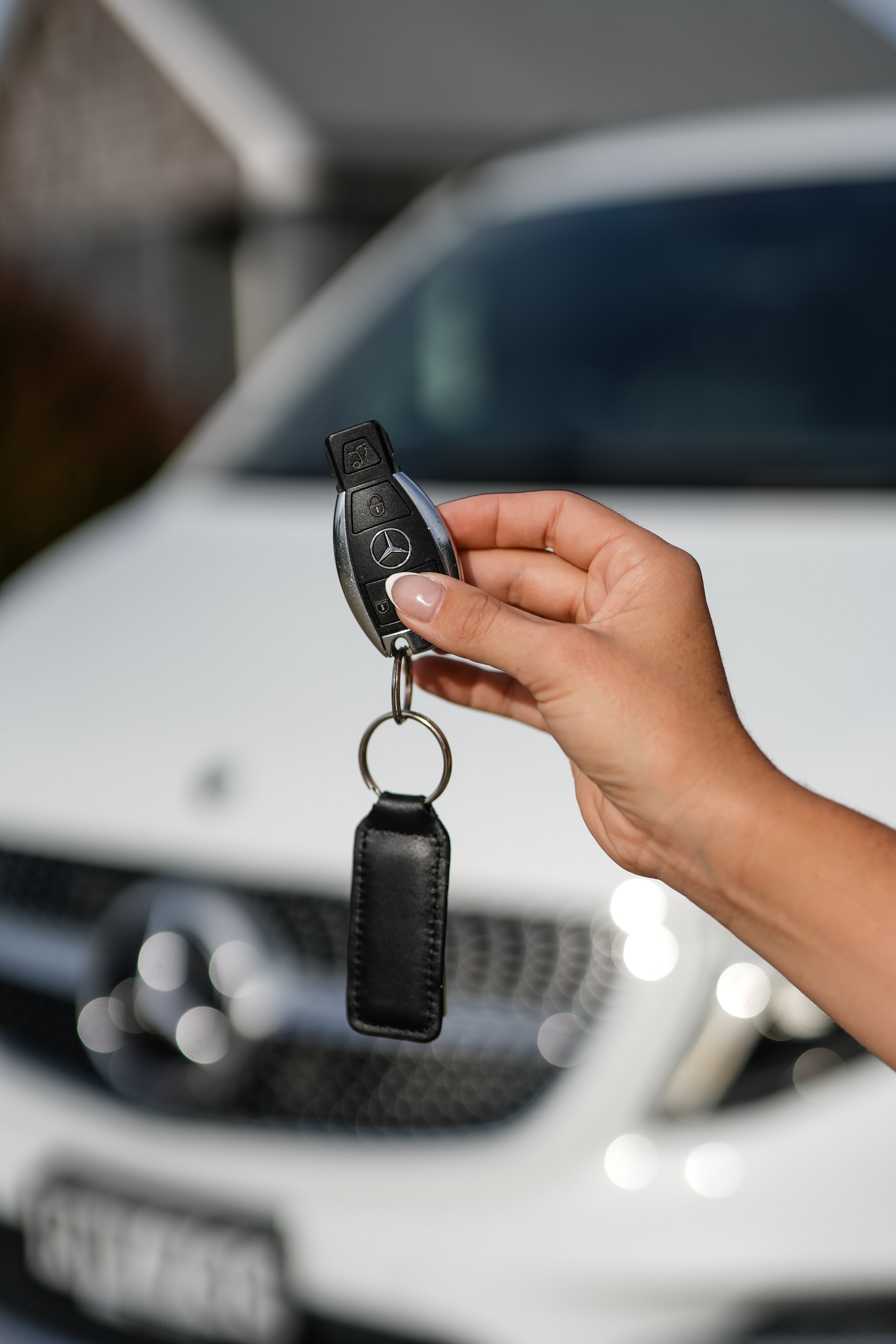 Close-up of a person holding a Mercedes-Benz car key with a keychain in front of a white vehicle.