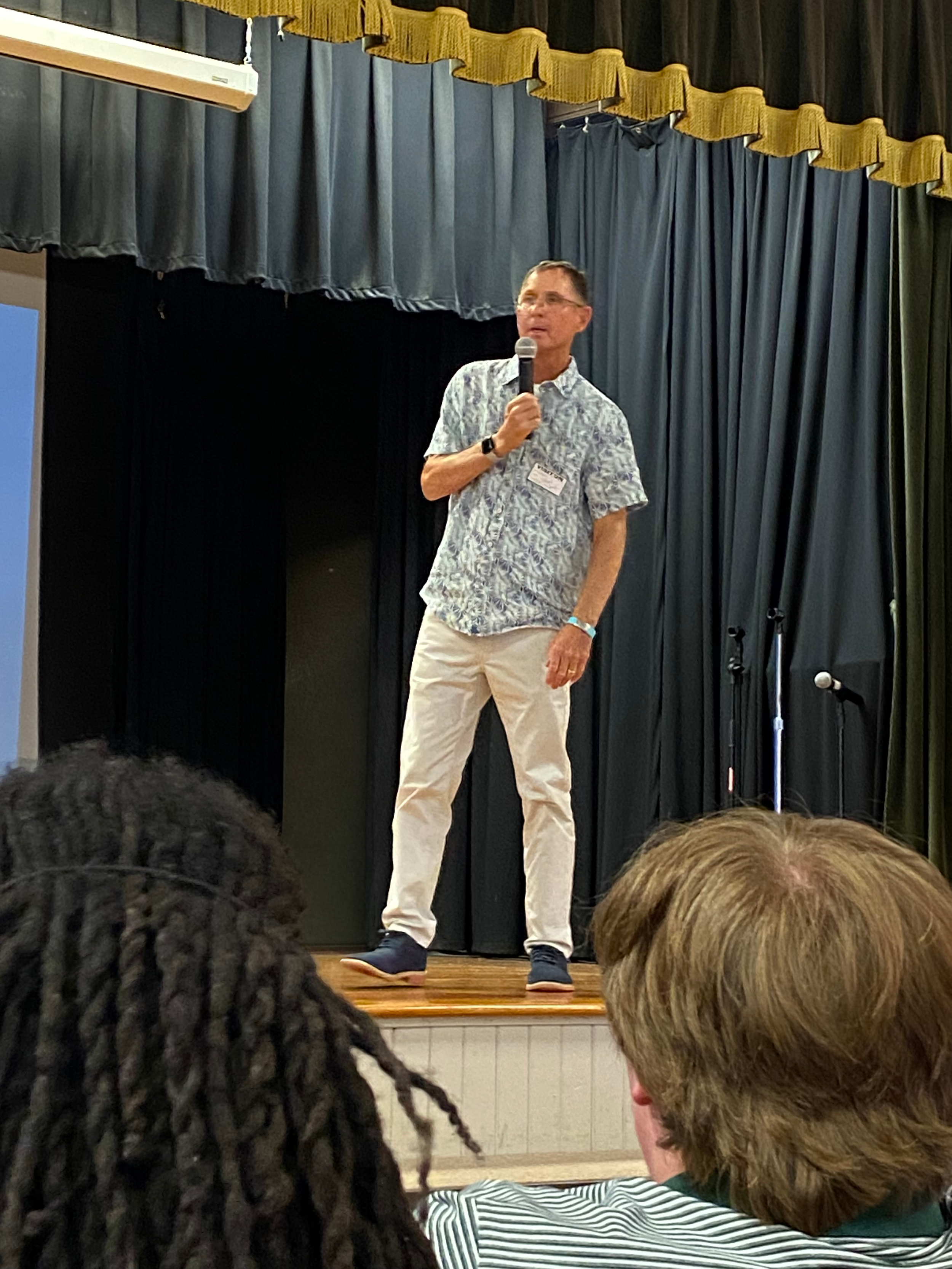 Michael J. Bowen speaking on stage in front of students from various colleges.