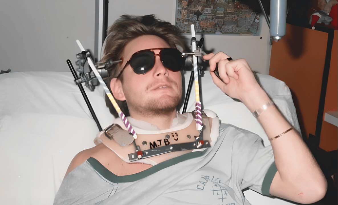 Michael J. Bowen lying in a hospital bed wearing sunglasses and headgear with medical equipment.