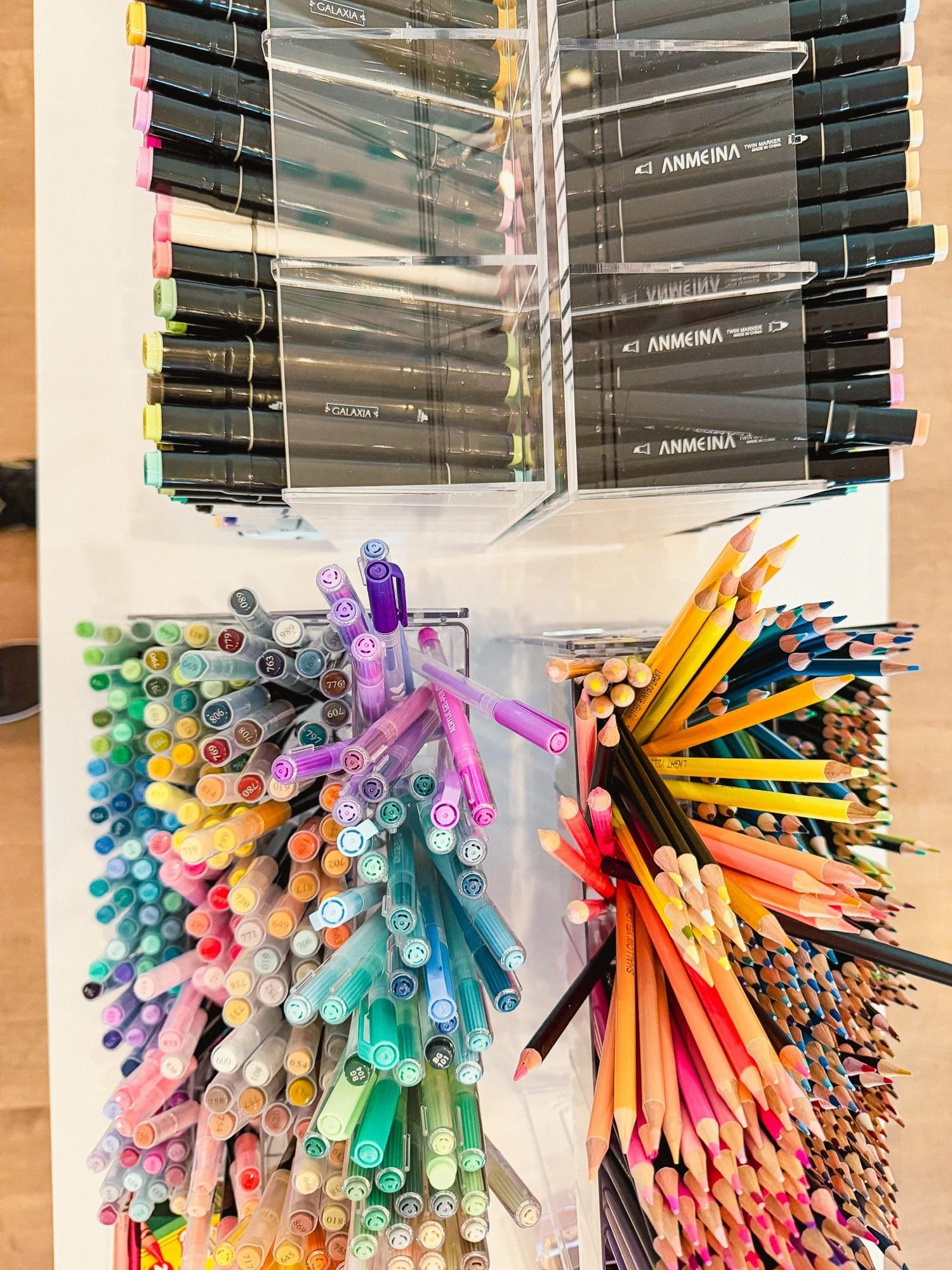 Colorful markers, pens, and colored pencils organized in a display case, viewed from above.