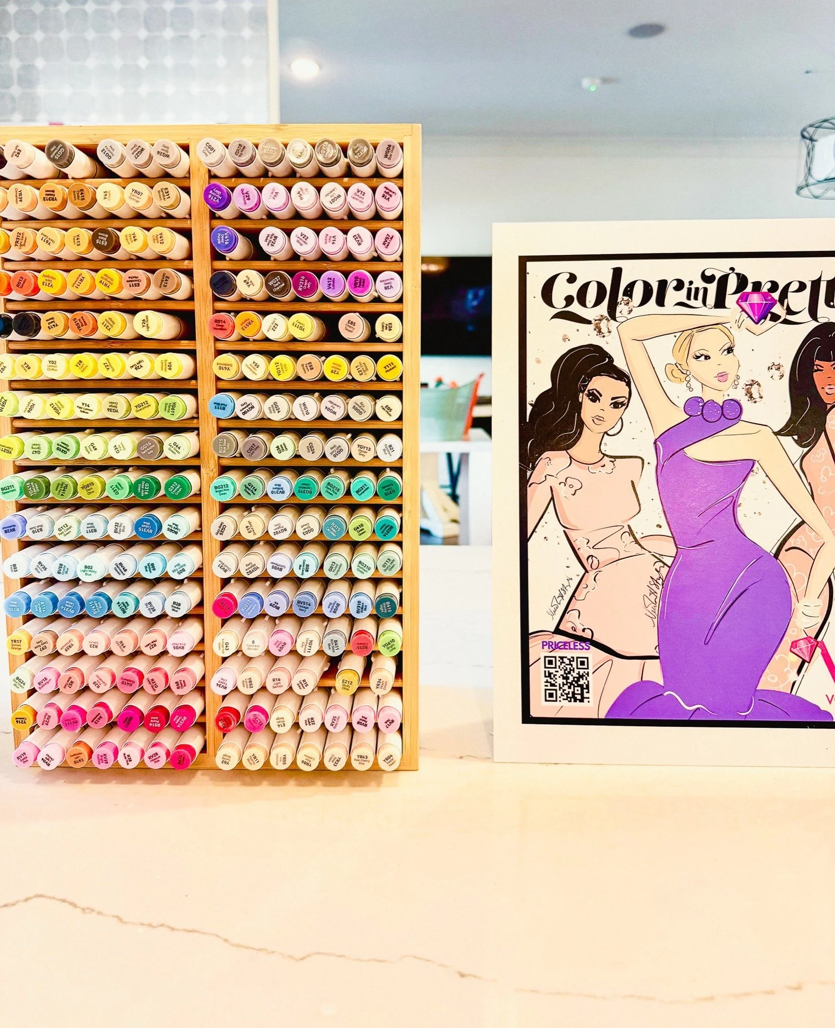 A display of multiple colorful markers organized in a wooden rack next to a sign with comic illustrations of women and the text 'Color in purse'.