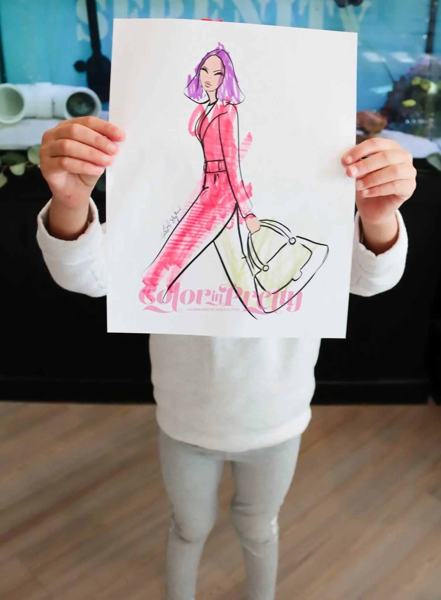 Person holding a drawing of a fashionable woman with purple hair and a pink outfit.