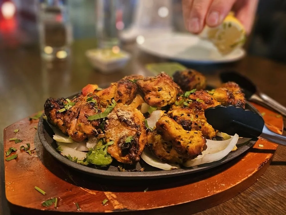 Grilled chicken pieces garnished with chopped cilantro on a sizzling hot plate with onions underneath, on a wooden serving board.