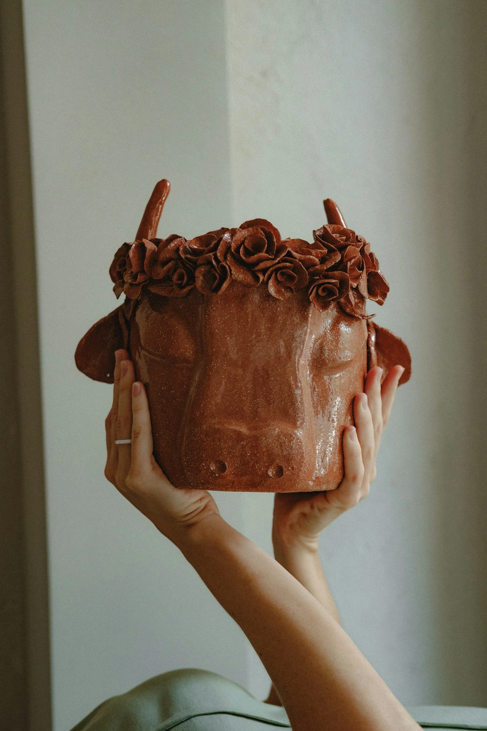 A person holding a large, decorated, chocolate-colored cake with rose-shaped frosting on top and chocolate sticks.