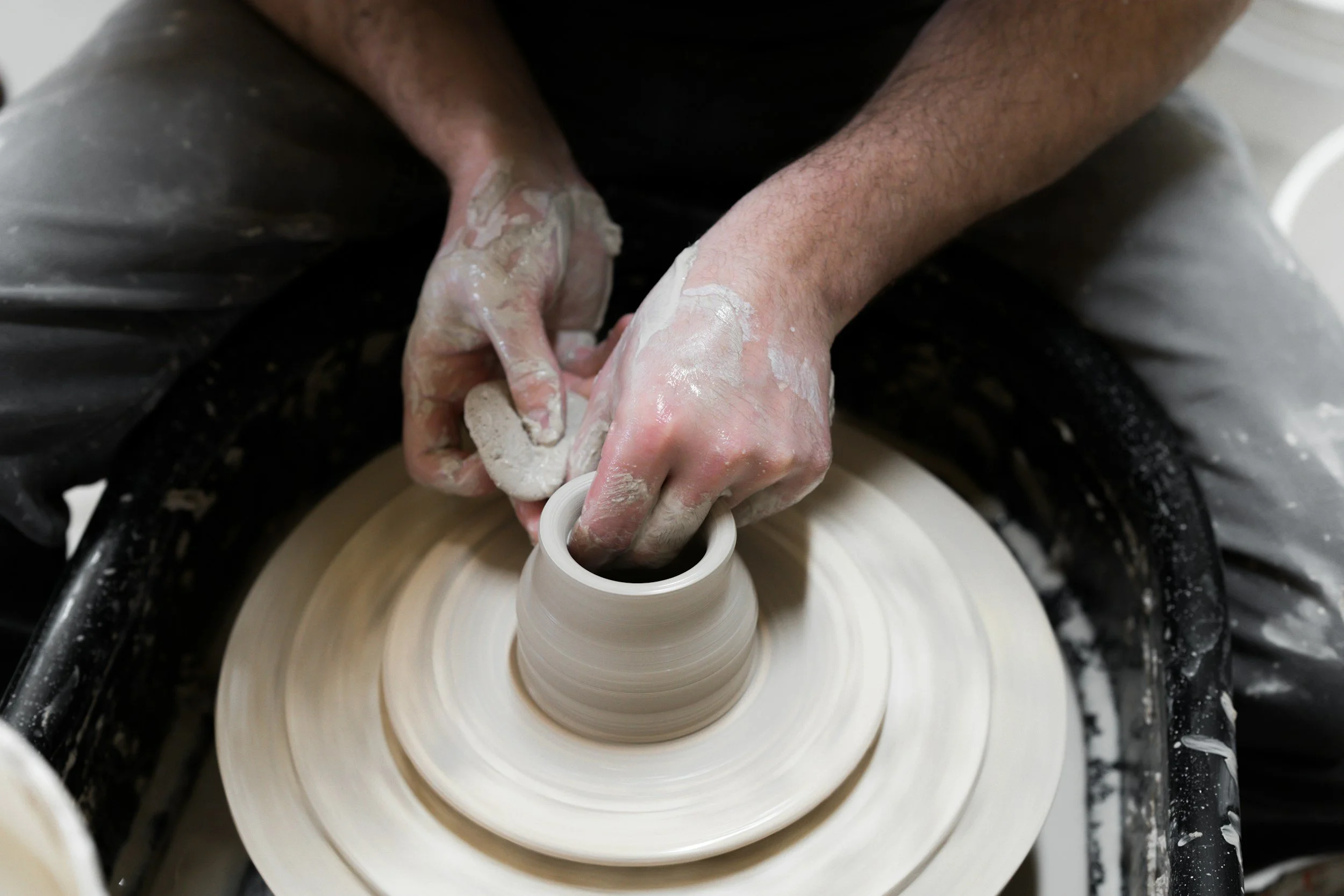 A person shaping clay on a pottery wheel with their hands covered in clay.