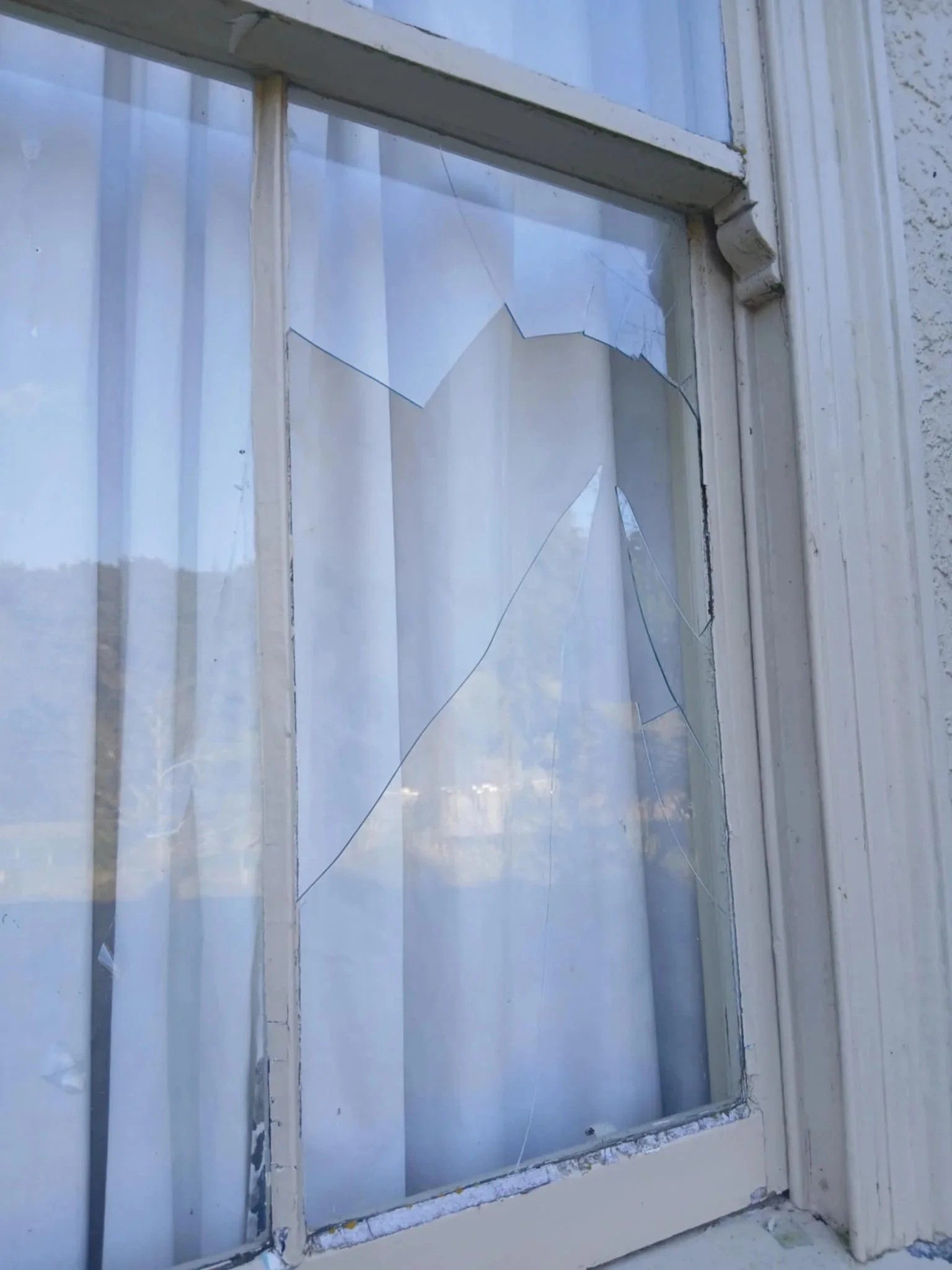 Broken window with shattered glass panes in a white window frame, set in an exterior wall.