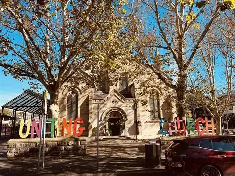 A church with large trees in front and colorful letters spelling 'Uniting Church' outside.