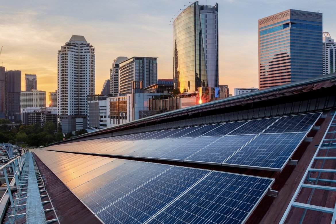 Solar panels covering a rooftop with a modern city skyline at sunset