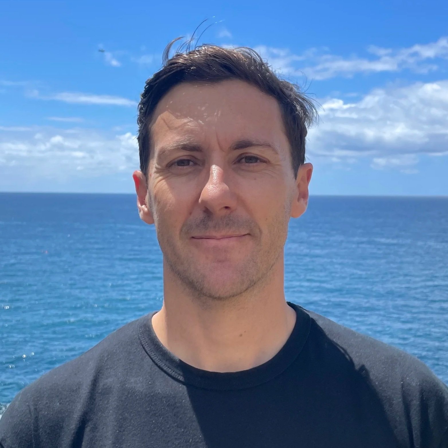 Man taking a selfie in front of the ocean under a bright blue sky