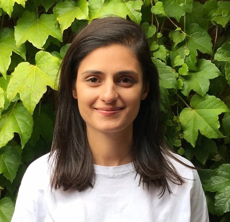 Smiling woman with long dark hair wearing a white shirt in front of green ivy leaves