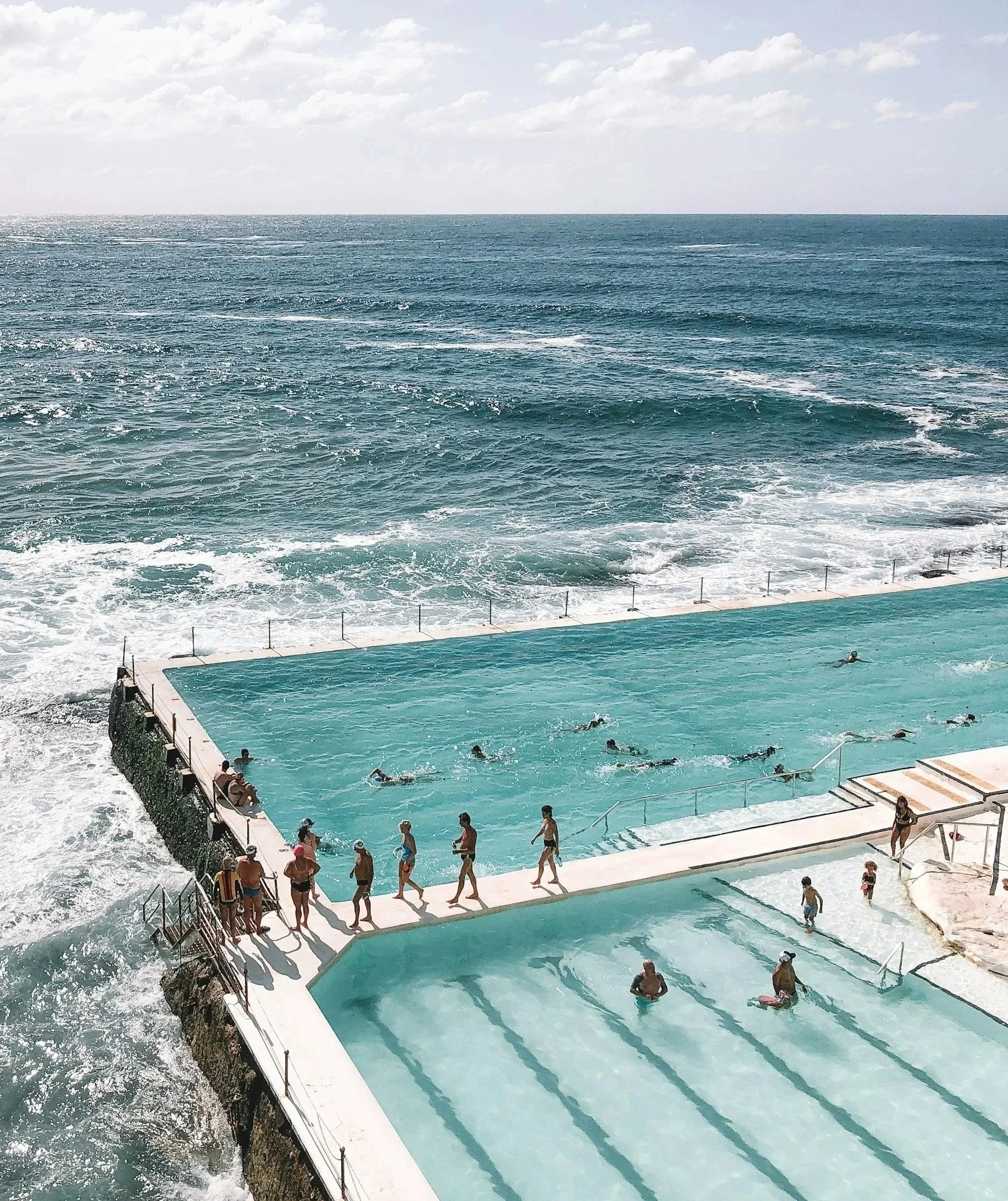 Swimmers in an oceanfront pool overlooking waves and the open sea