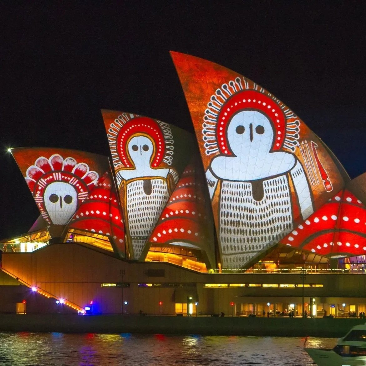 Sydney Opera House illuminated at night with colorful Aboriginal-inspired projections reflected in the harbor