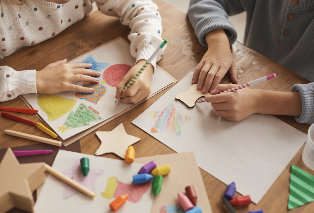 Children drawing and coloring holiday-themed pictures with markers and crayons at a wooden table.