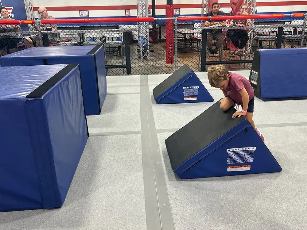 Young child climbing over a low padded obstacle during Little Ninjas