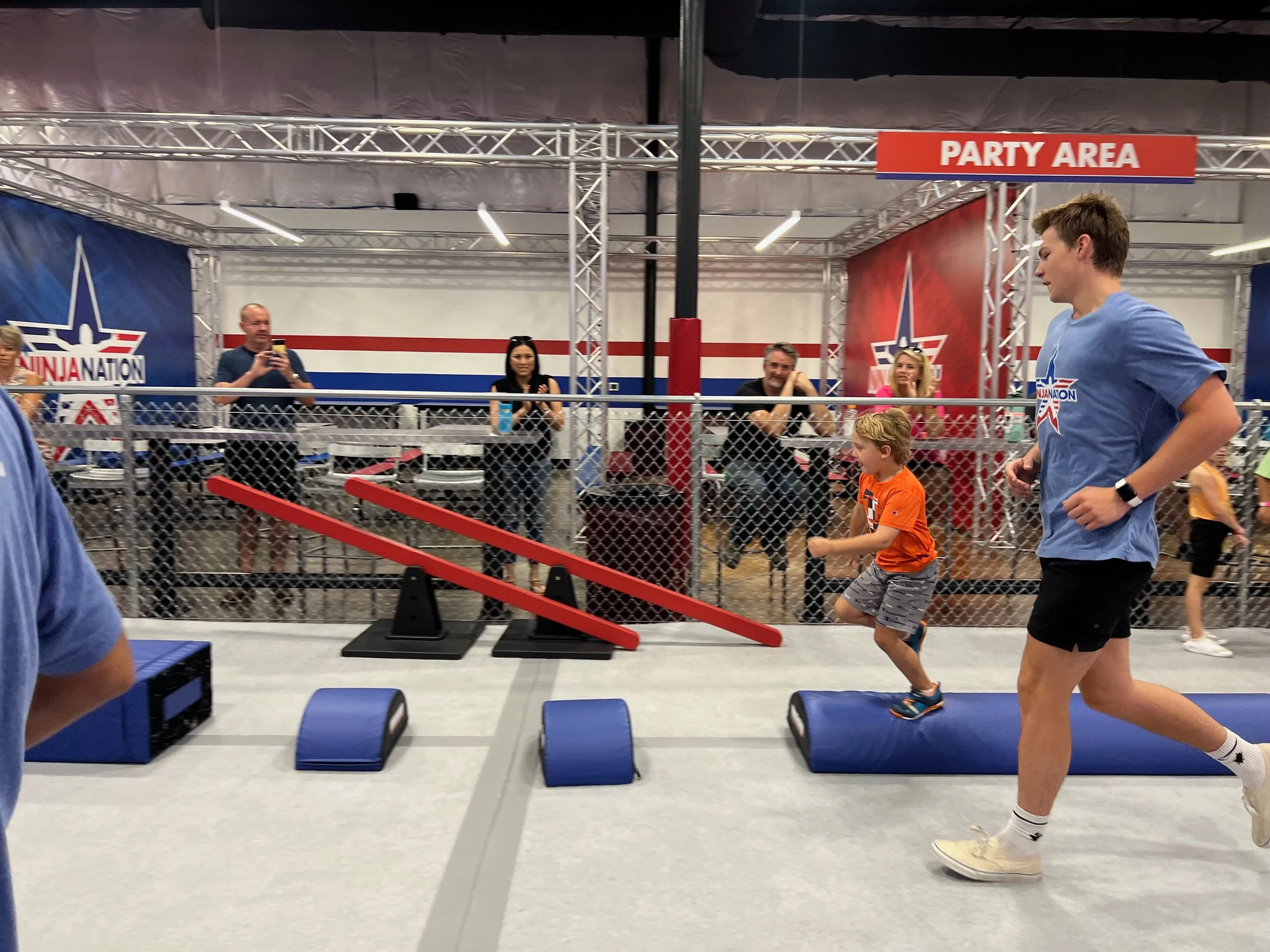 People participating in a fitness class at a gym with a sign that says 'Party Area' and a mural with a star and stripes design.