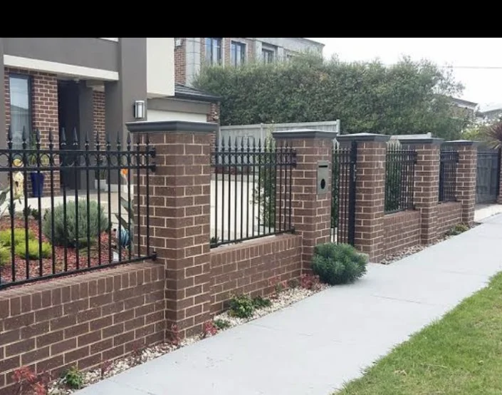 Brick fence with black metal fencing and gate along a sidewalk in front of a residential building.