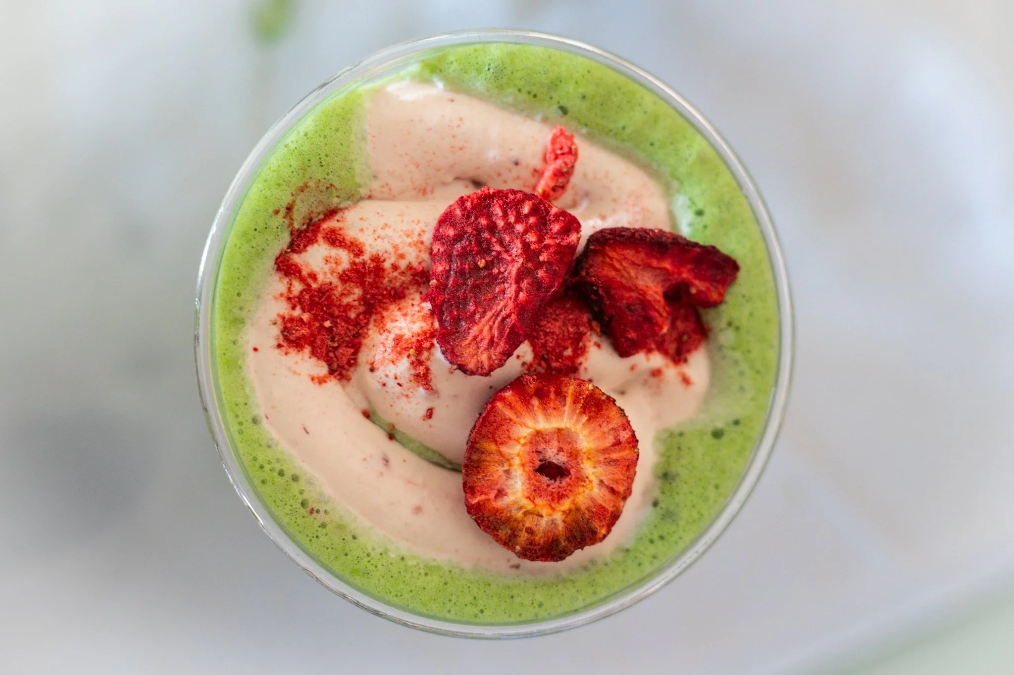 Overhead view of a green smoothie topped with slices of strawberries.