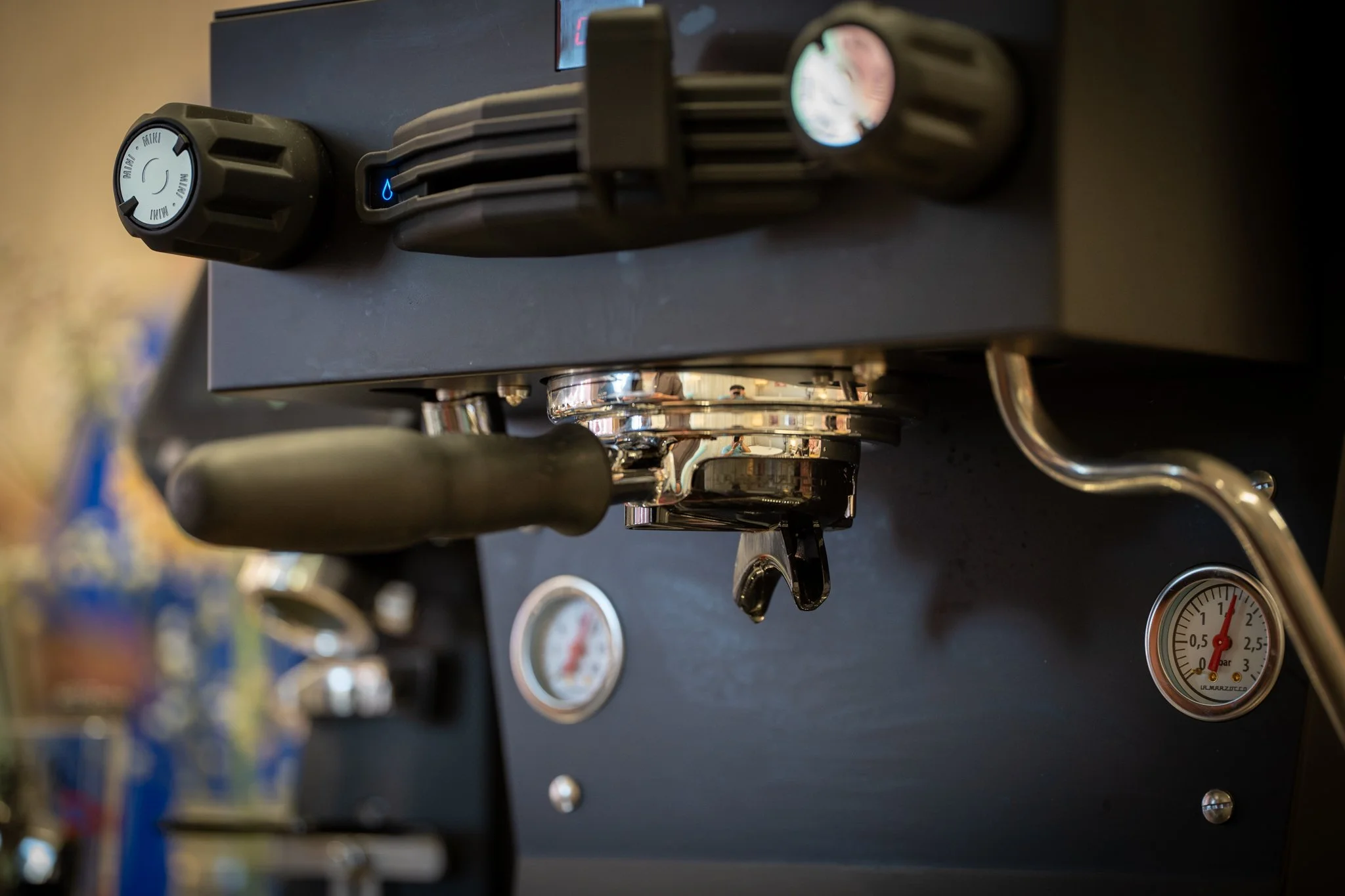 Close-up of a black espresso machine with gauges, a steam wand, and control knobs.