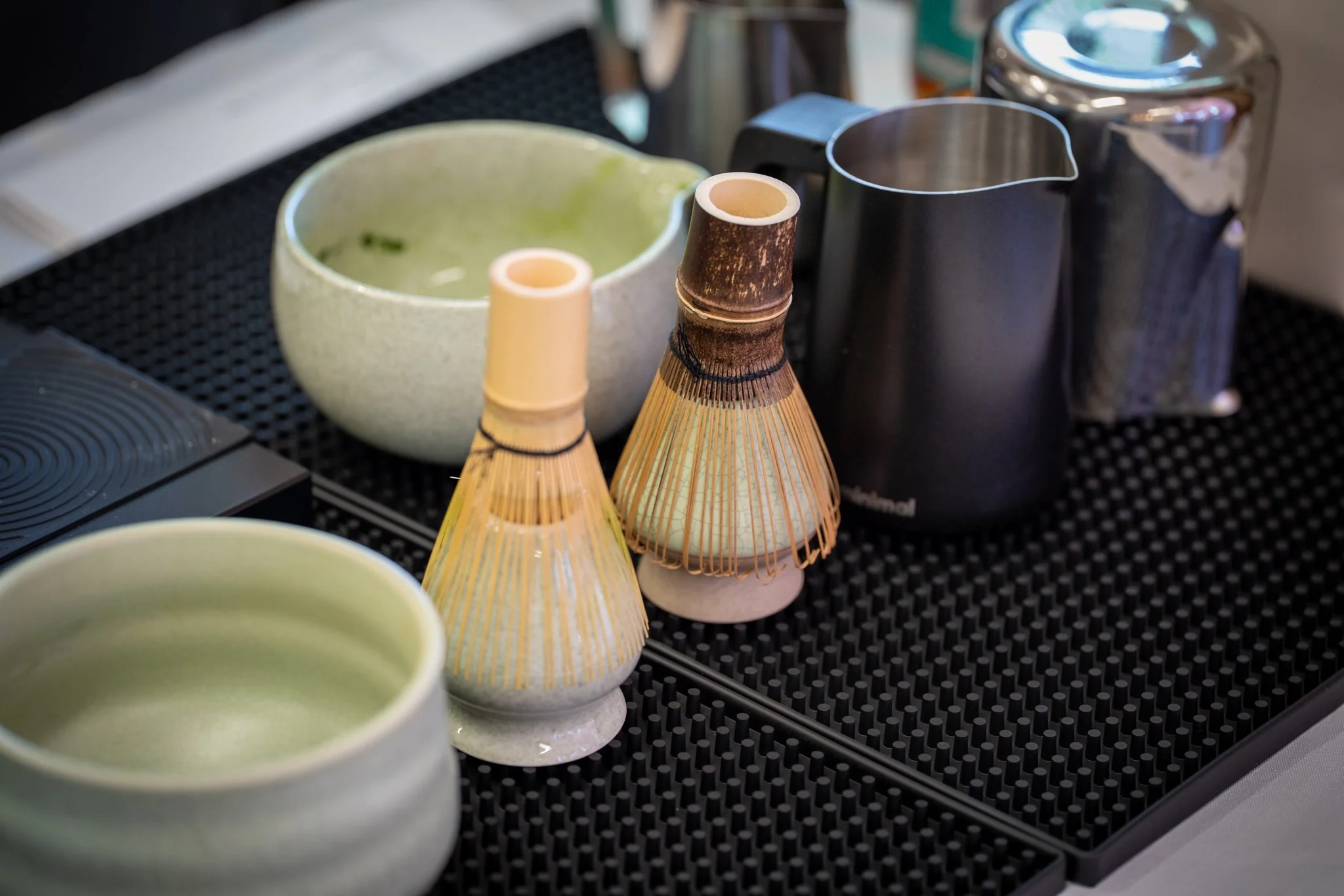 Tea cups and teapots on a black textured surface, some cups are light green and ceramic, and the teapots are made of bamboo and metal.