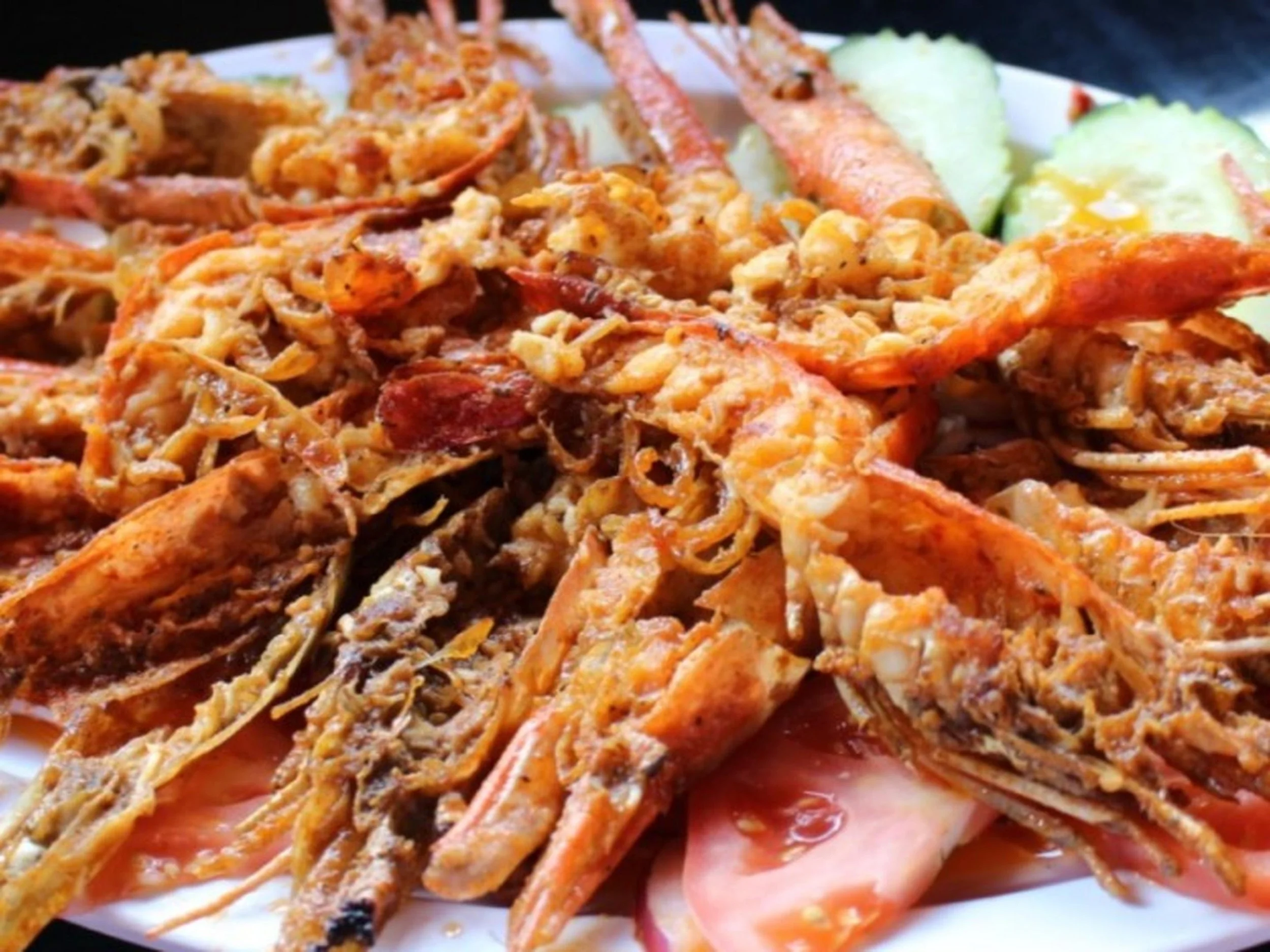 A plate of assorted seafood, including cooked shrimp and crab, garnished with slices of cucumber and some sliced meat or ham.