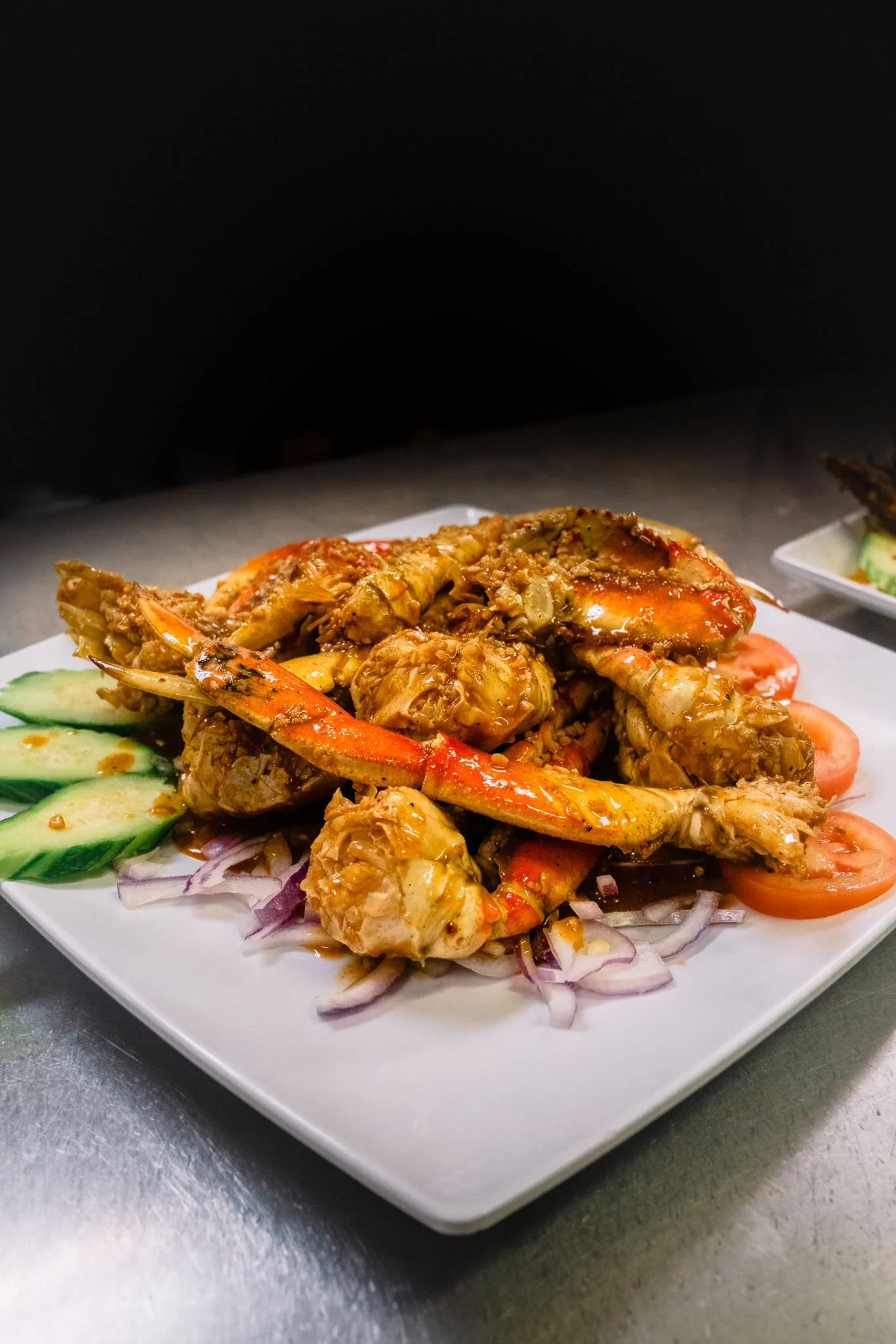 Cooked shrimp and chicken curry served with sliced cucumbers, tomatoes, and onions on a white plate.