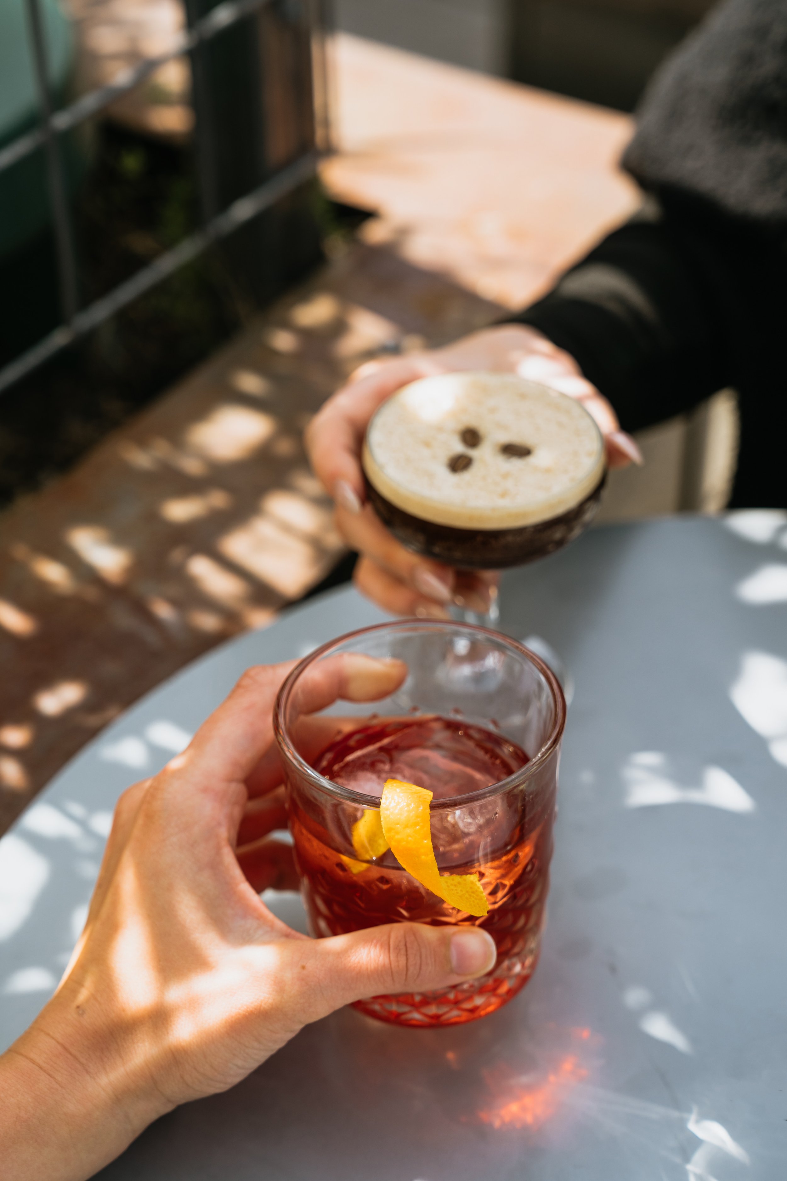 Two hands holding a negroni and an espresso martini