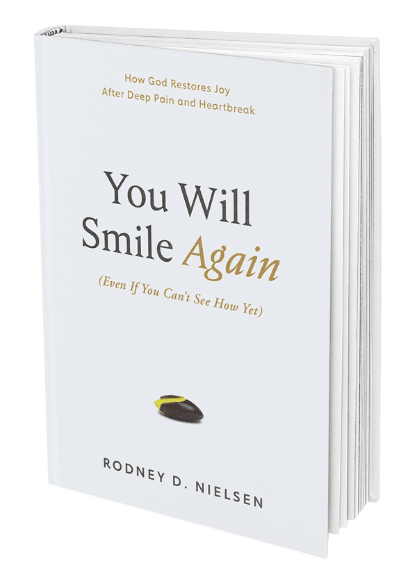 The hardback book cover: 'You Will Smile Again (Even If You Can't See How Yet)' by author and pastor Rodney D. Nielsen. Subtitle: How God Restores Joy After Deep Pain and Heartbreak. The cover is white except for a small seed beginning to grow.