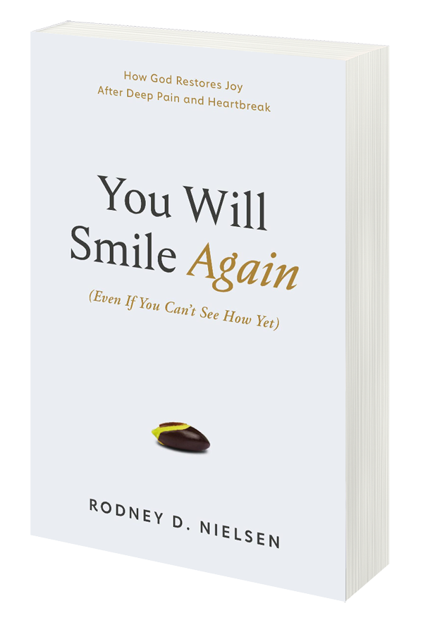 The paperback book cover: 'You Will Smile Again (Even If You Can't See How Yet)' by author and pastor Rodney D. Nielsen. Subtitle: How God Restores Joy After Deep Pain and Heartbreak. The cover is white except for a small seed beginning to grow.